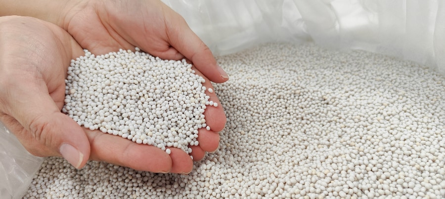 Hands holding recycled PET pellets above a bulk bag